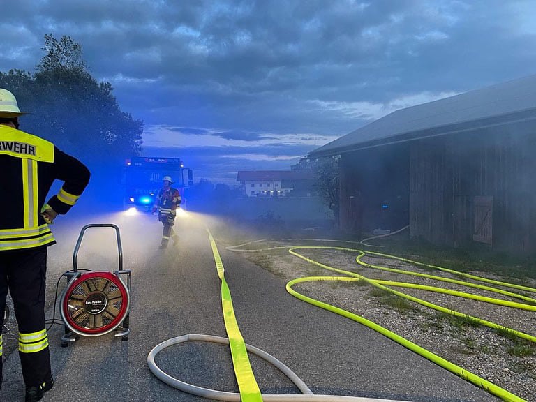 Feuerwehreinsatz bei nebligem Wetter, neongelbe Schläuche am Boden, blaue und weiße Blaulichter im Nebel, zwei Feuerwehrleute sichtbar